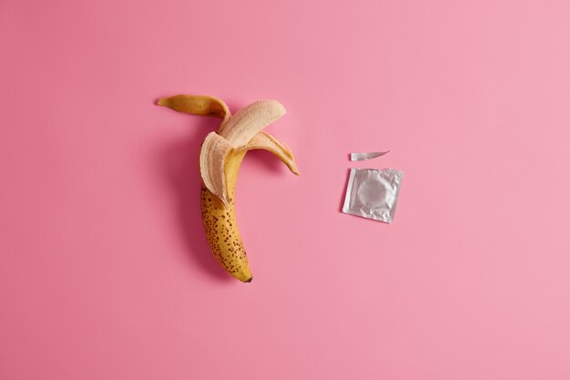 Condones sabrosos de alta calidad que se adaptan a tu estado de ánimo. Anticonceptivo de plátano sobre fondo rosa. Apetitoso producto de goma y fruta sin pelar para la intimidad. Método anticonceptivo. Concepto de seguridad.