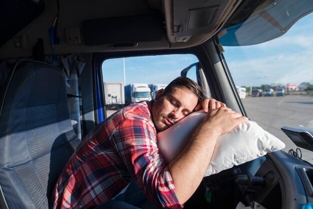 Conductor de camión cansado se inclinó sobre el volante durmiendo en su almohada