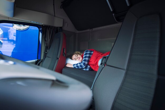 Conductor de camión durmiendo en la cama dentro del interior de la cabina del camión