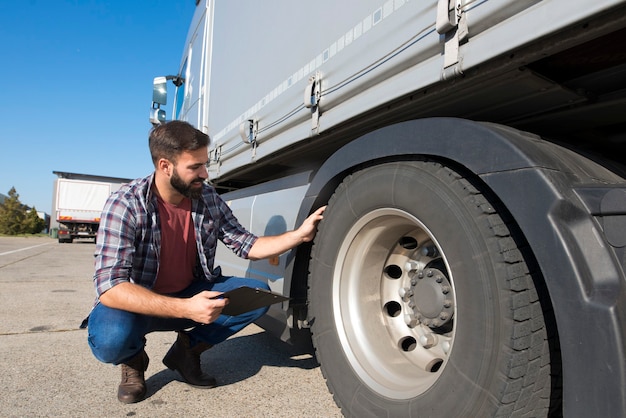 Foto gratuita conductor de camión inspeccionando neumáticos y comprobando la profundidad de la banda de rodadura del neumático para una conducción segura