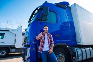 Foto gratuita conductor de camión profesional delante del vehículo de transporte largo sosteniendo los pulgares hacia arriba listo para un nuevo viaje