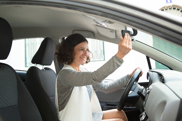 Conductor de coche femenino alegre que mira en espejo