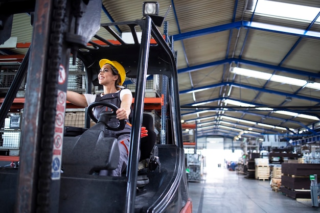 Conductor industrial femenino operando la máquina montacargas en el almacén de la fábrica