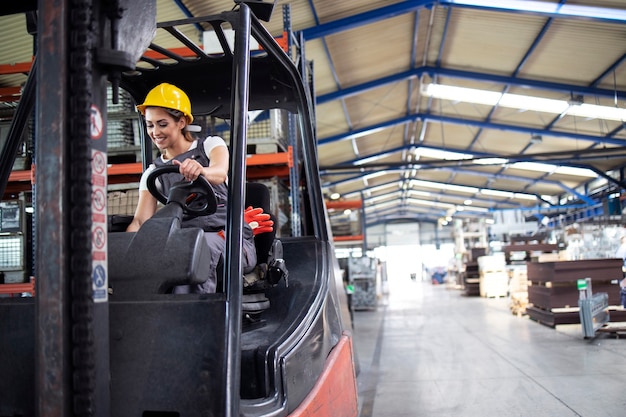 Conductor industrial femenino profesional operando la máquina elevadora en el almacén de la fábrica