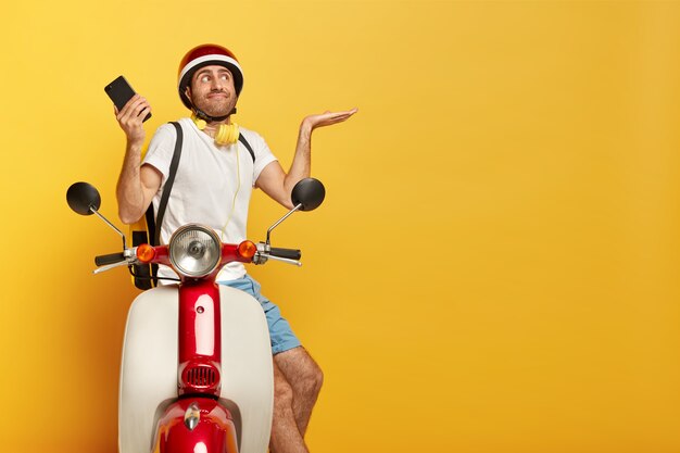 Conductor masculino guapo confundido en scooter con casco rojo