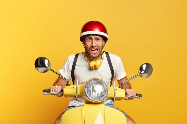 Conductor masculino guapo disgustado en scooter con casco rojo