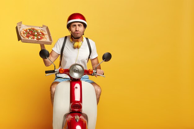 Conductor masculino guapo con propósito en scooter con casco rojo entregando pizza