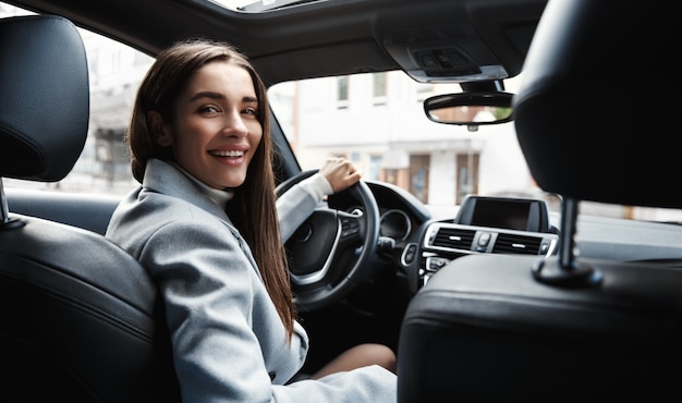 Conductor de mujer elegante mirando el asiento trasero, sonriendo feliz