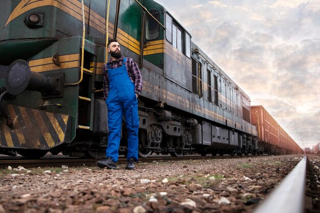 Conductor de tren de pie junto a la locomotora en la estación de ferrocarril