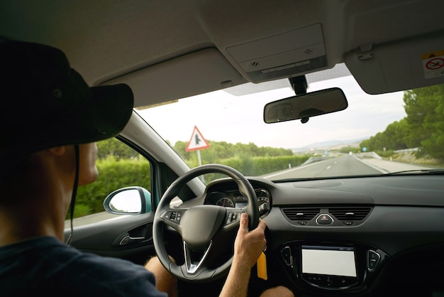 El conductor viaja en su automóvil por la autopista, vista desde el interior del automóvil. Manos en el volante, clima frío de verano
