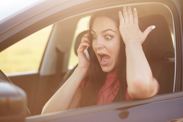 La conductora no sabe cómo reparar el automóvil, llama al esposo por teléfono celular, mira con sorpresa y miedo