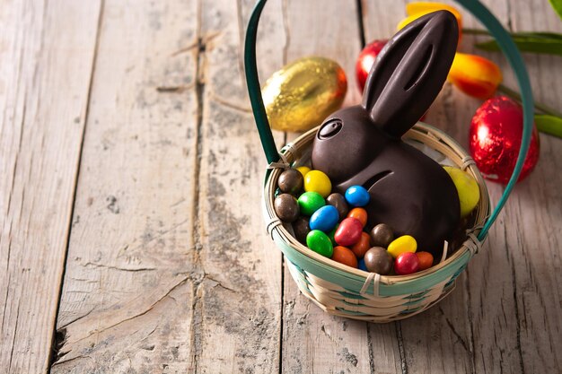 Conejito de chocolate de Pascua y huevos coloridos en la mesa de madera