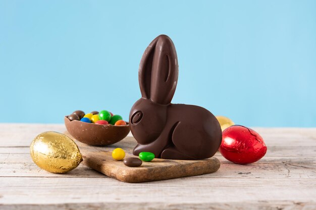 Conejito de chocolate de pascua y huevos coloridos sobre mesa de madera y fondo azul