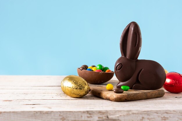 Conejito de chocolate de pascua y huevos coloridos sobre mesa de madera y fondo azul