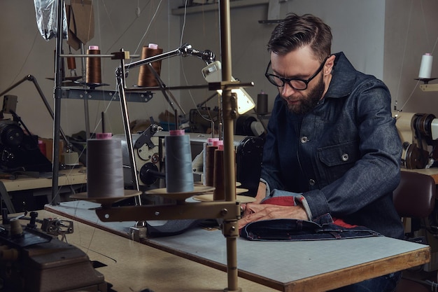 Confeccionando ropa "o" Fabricando ropa. sastre sentado a la mesa y trabajando en una máquina de coser en un taller de costura.