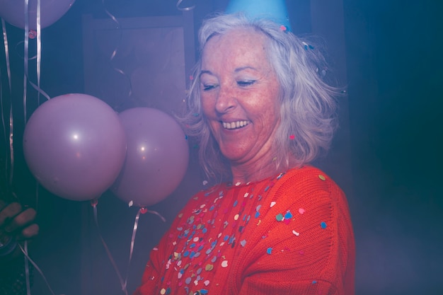 Confeti colorido sobre la mujer mayor sonriente con globos rosados