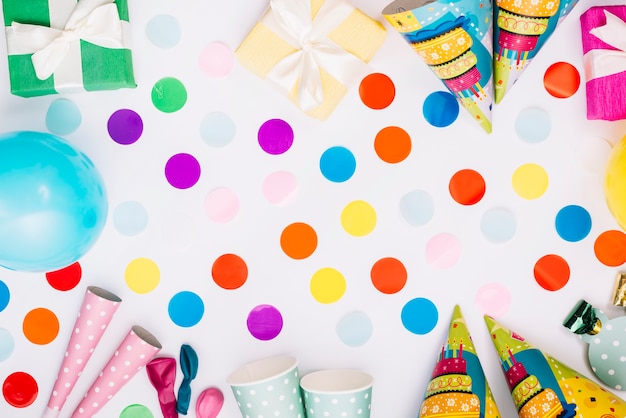 Confeti de globos con cajas de regalo; sombrero de fiesta; cuerno; vaso desechable sobre fondo blanco