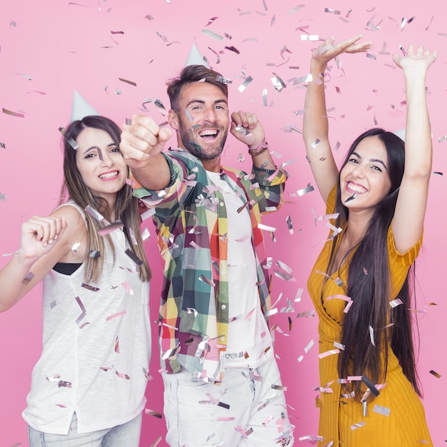 Foto gratuita confeti de plata cayendo sobre los amigos bailando sobre fondo rosa