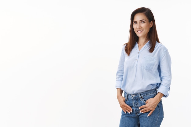 Confiada y guapa esposa lanza la puesta en marcha, toma las manos de los bolsillos de los jeans, gira al frente complacido, seguro de sí mismo, victoria asertiva, decidido a lograr el mejor resultado, párate feliz en la pared blanca