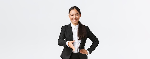 Confiada y sonriente mujer de negocios asiática extiende la mano para un firme apretón de manos saludando al cliente o socio comercial para firmar un acuerdo con un fondo blanco determinado y listo