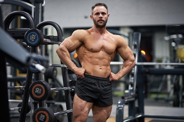 Foto gratuita confiado culturista barbudo posando con las manos en la cintura en el gimnasio retrato de un fuerte caucásico