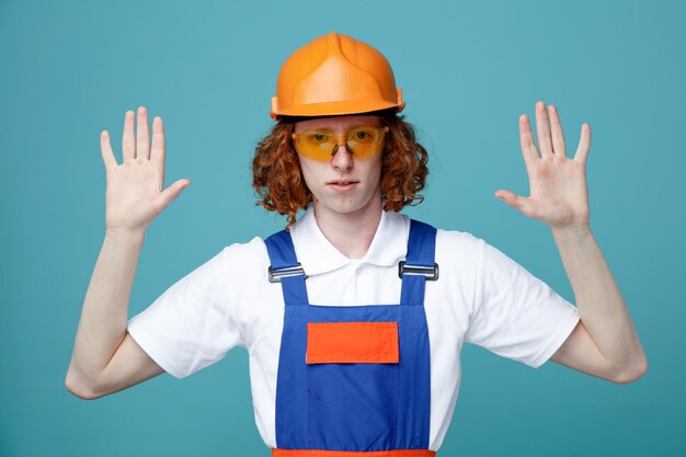 Confiado extendiendo las manos joven constructor hombre en uniforme aislado sobre fondo azul.