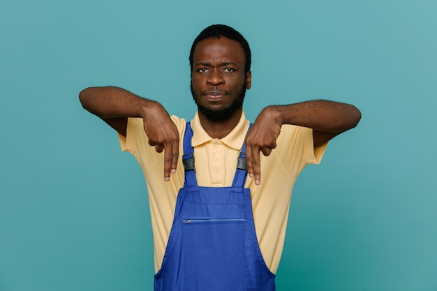 Confiado fingiendo sostener algo joven afroamericano limpiador masculino en uniforme aislado sobre fondo azul.