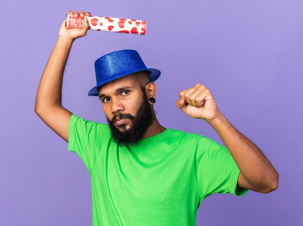 Confiado joven afroamericano con sombrero de fiesta sosteniendo cañón de confeti mostrando gesto de sí
