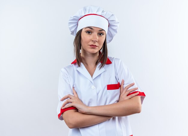 Confiado joven cocinera vistiendo uniforme de chef cruzando las manos aisladas sobre fondo blanco.