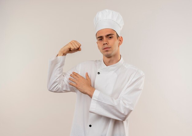 Confiado joven cocinero vistiendo uniforme de chef haciendo un gesto fuerte en la pared blanca aislada con espacio de copia