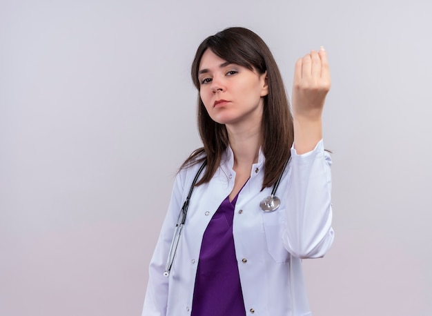 Confiado joven doctora en bata médica con estetoscopio sostiene la mano sobre fondo blanco aislado con espacio de copia