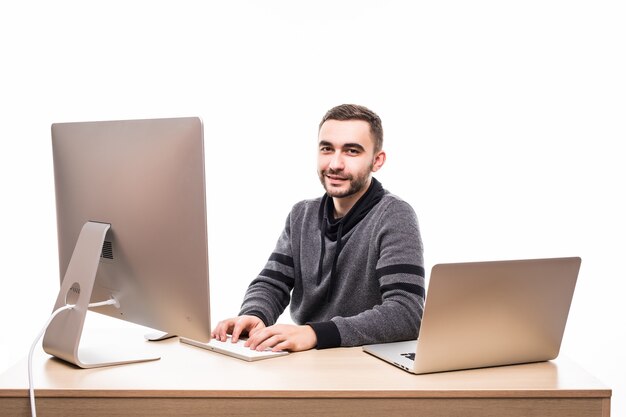 Confiado joven empresario sentado en la mesa con ordenador portátil y pc, mirando a cámara aislada en blanco