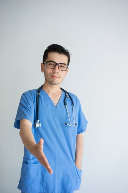 Confiado joven médico extendiendo el brazo para el apretón de manos. Concepto de médico amigable.