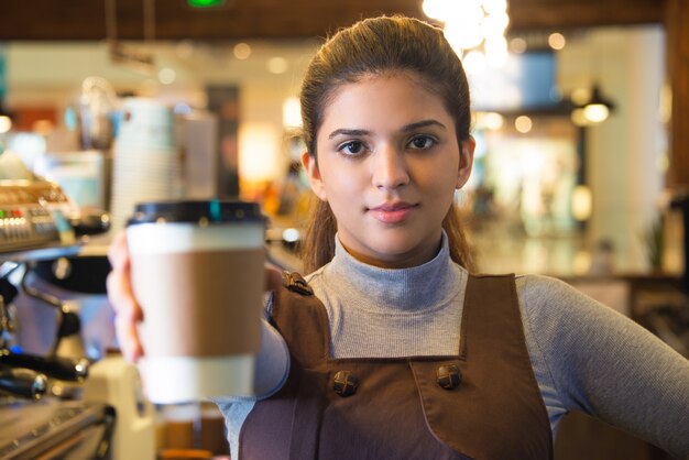 Confiado joven mujer café barista dando taza