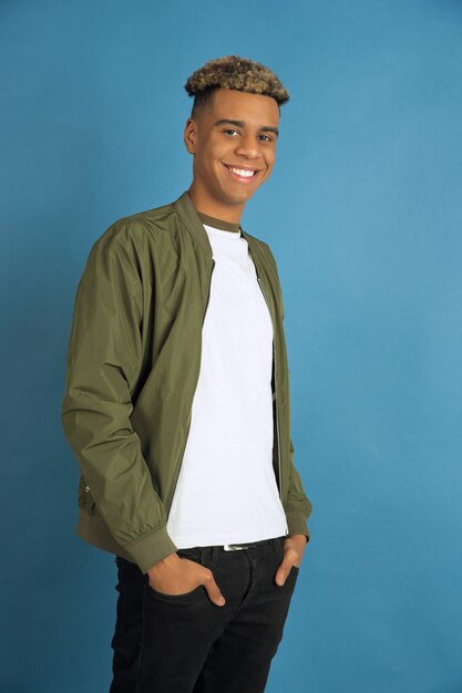 Confiado y sonriente. Retrato de hombre afroamericano aislado sobre fondo azul de estudio. Hermoso modelo masculino en ropa casual. Concepto de emociones humanas, expresión facial, ventas, publicidad. Copyspace.