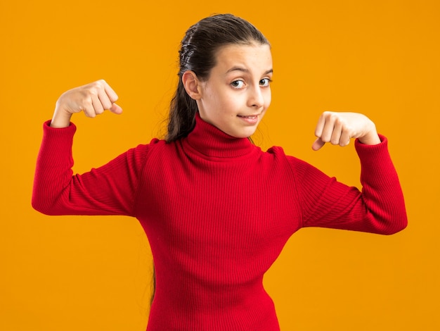 Confianza adolescente mirando al frente haciendo un gesto fuerte aislado en la pared naranja