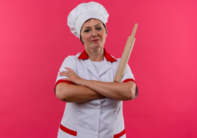 Foto gratuita confianza cocinera de mediana edad en uniforme de chef sosteniendo un rodillo cruzando las manos en la pared rosa aislada