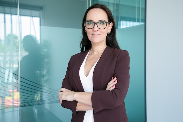 Foto gratuita confianza empresaria positiva vistiendo traje formal y gafas, de pie con los brazos cruzados y sonriendo