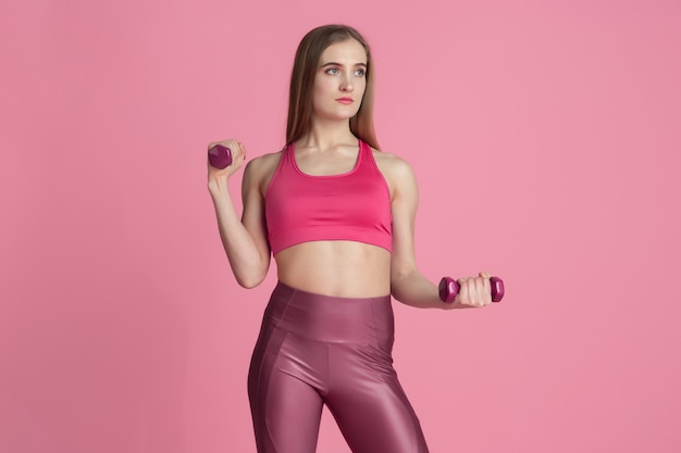Confianza. Hermosa joven atleta practicando, retrato rosa monocromo. Modelo caucásico de ajuste deportivo con pesas. Culturismo, estilo de vida saludable, concepto de belleza y acción.