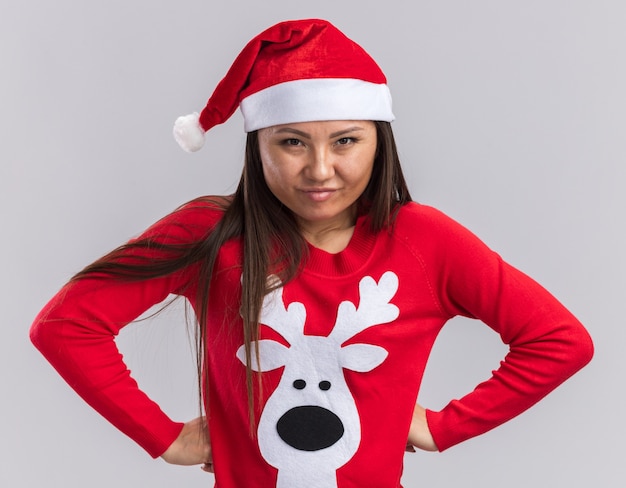 Foto gratuita confianza joven asiática vistiendo gorro de navidad con suéter poniendo las manos en las caderas aisladas sobre fondo blanco