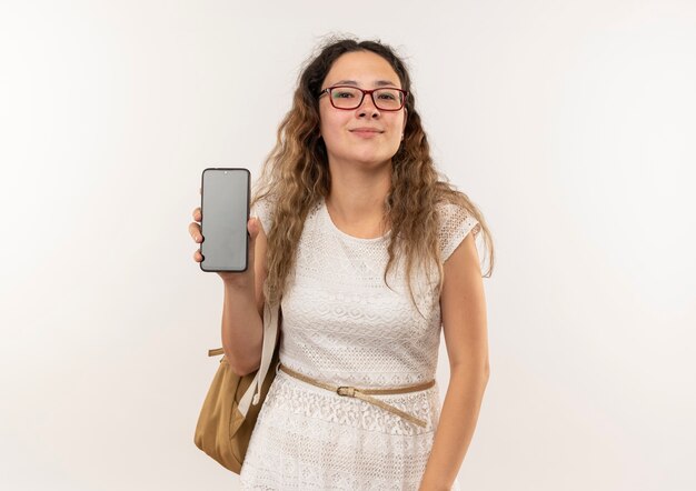 Confianza joven colegiala bonita con gafas y bolso trasero mostrando teléfono móvil aislado en blanco con espacio de copia