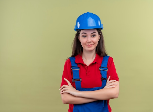 Confianza joven constructor con casco de seguridad azul de brazos cruzados sobre fondo verde aislado con espacio de copia