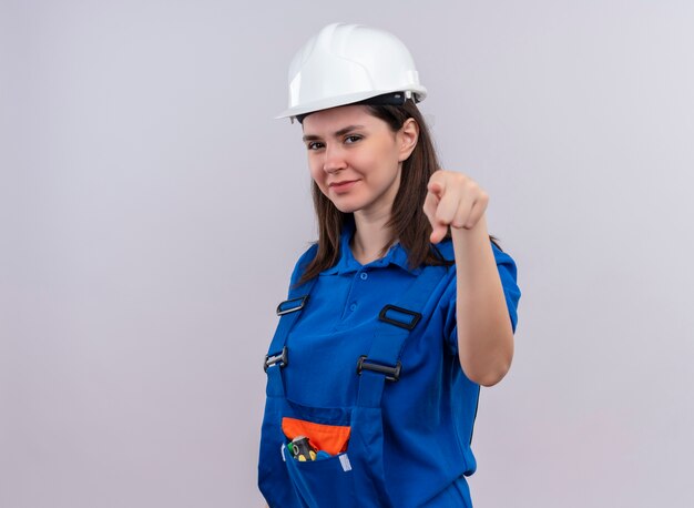 Confianza joven constructor con casco de seguridad blanco y puntos de uniforme azul en la cámara sobre fondo blanco aislado con espacio de copia