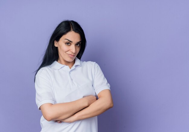 Confianza joven morena caucásica se encuentra con los brazos cruzados mirando aislado en la pared púrpura