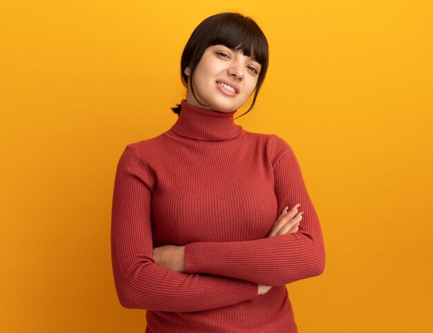 Confianza joven morena caucásica se encuentra con los brazos cruzados en naranja