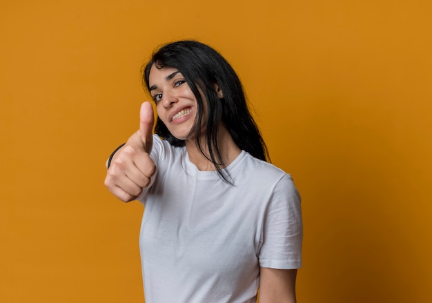 Confianza joven morena caucásica pulgares arriba aislados en la pared naranja