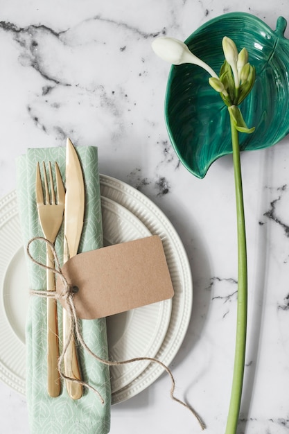 Configuración de lugar con placas blancas; Servilleta doblada y cubiertos con flores blancas.