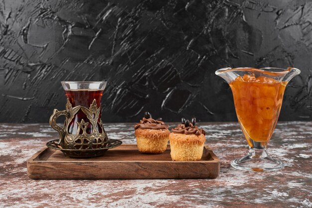 Confitura, magdalenas y un vaso de té en una tabla de madera.
