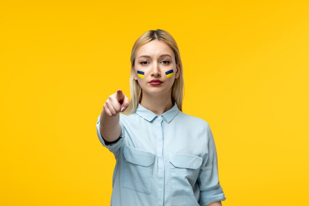 Conflicto ucraniano ruso linda chica fondo amarillo con bandera ucraniana en las mejillas señalando con el dedo