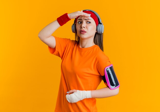 Confundida joven deportiva con diadema y muñequeras y auriculares